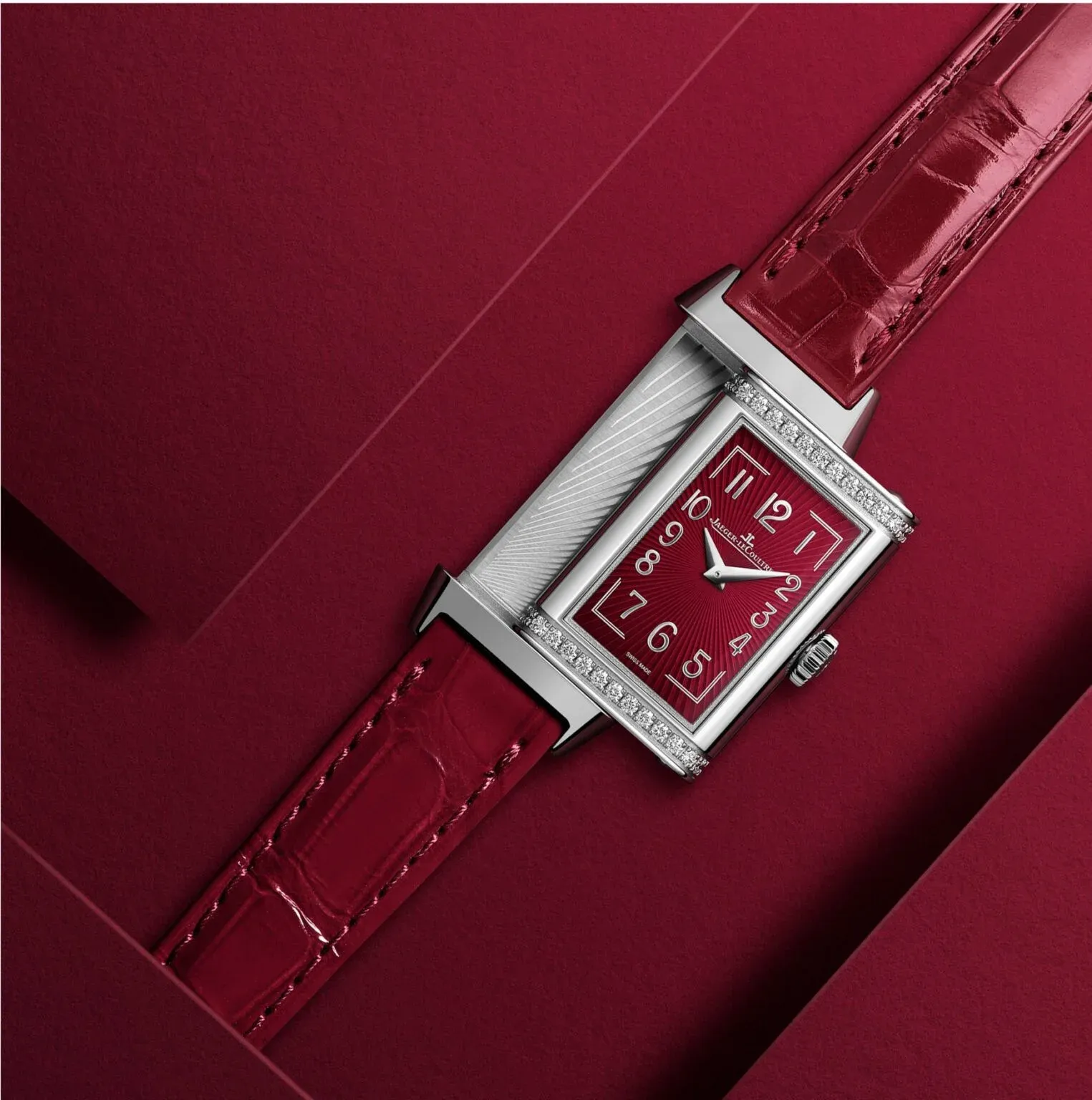 Jaeger-LeCoultre Reverso watch with a red dial, diamond-set bezel, and red leather strap against a deep red background.